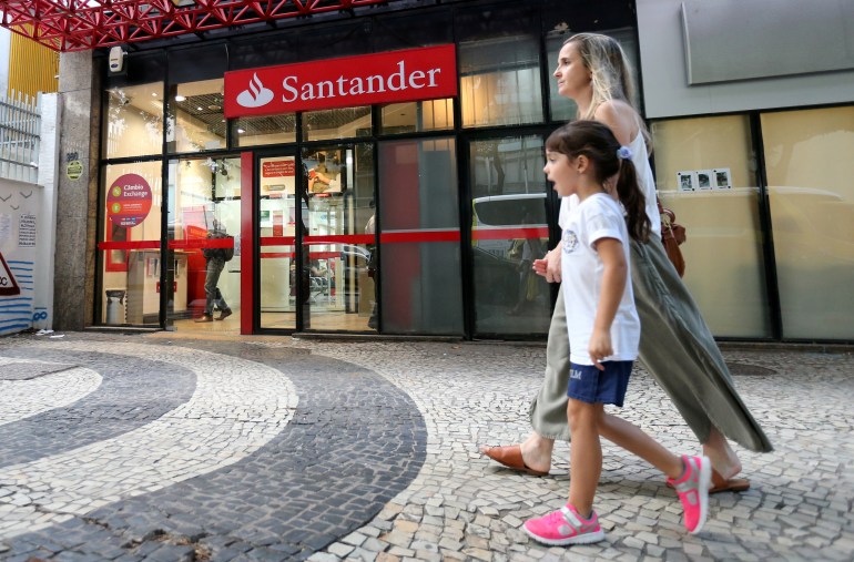 A woman and a child walk past a Banco Santander branch in Rio de Janeiro, Brazil