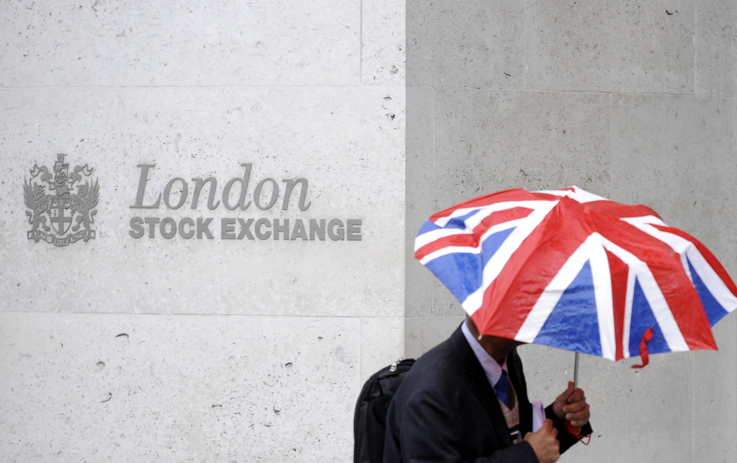 A worker shelters from the rain as he passes the London Stock Exchange in London