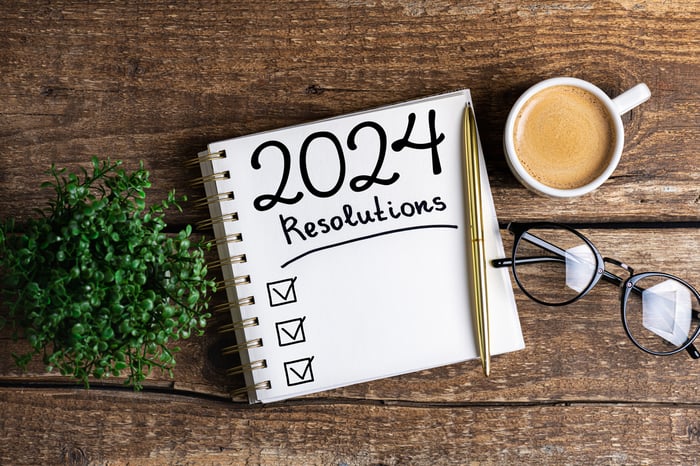 A notepad with "2024 resolutions" written on it sits on a table with a cup of coffee.