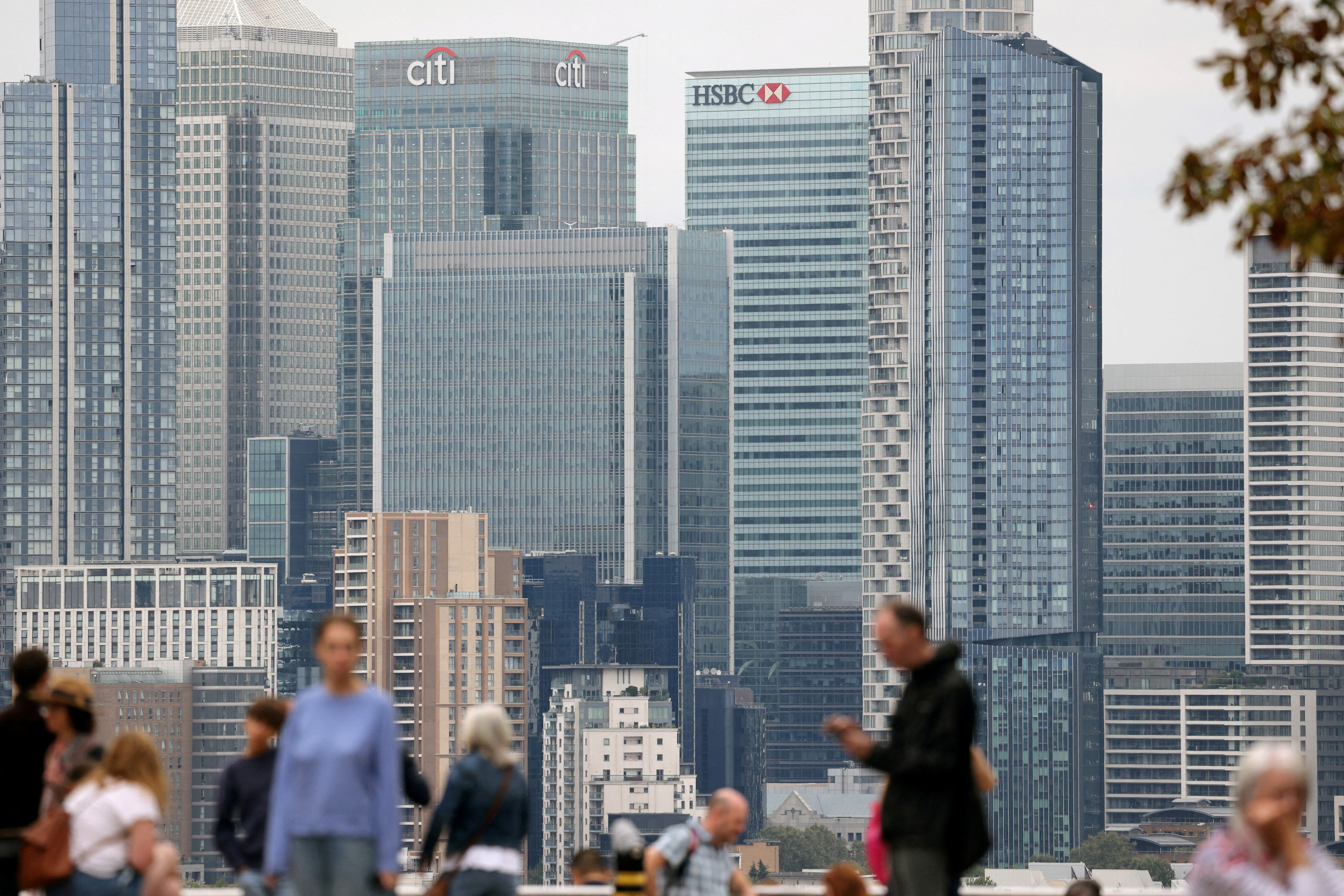 People stand in Greenwich Park with the Canary Wharf financial district in the distance