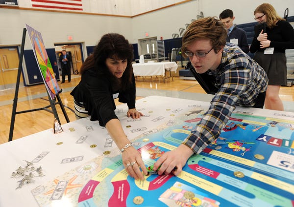 Cape Cod Five Wellfleet branch manager Patty Foster, left, helps high school senior Sam McCormack of Harwich place a piece on the Game of Reality in a hands-on financial literacy role-playing event at Monomoy Regional High School in 2016. A bill being debated in the state house would require all high school students to take a course on financial literacy in order to graduate.