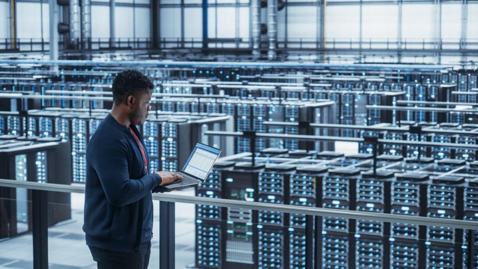 A person working on a laptop overlooking a data center. 