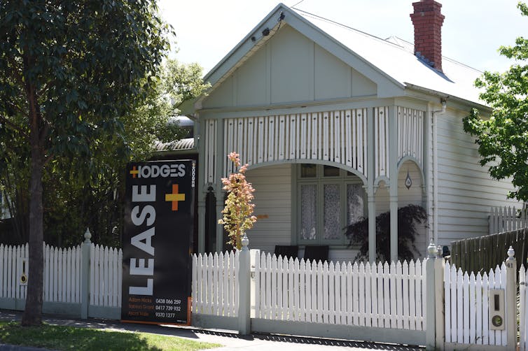 Small grey and white house with a Lease sign attached to the front fence