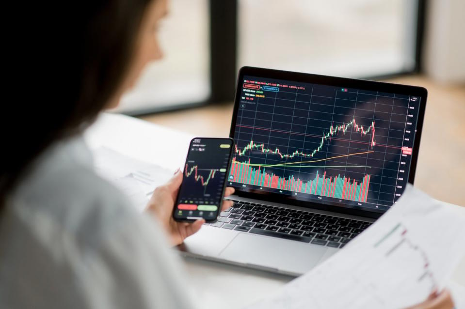 A person looks at a stock chart on their phone and on a laptop. 