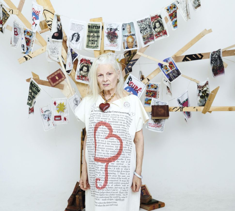 Woman with blonde hair and large white dress stands in front of hanging lines of playing cards