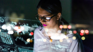 A businesswoman looks at a floating interface screen full of data.