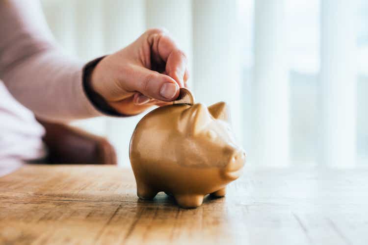 Woman putting a one euro coin in a golden piggy bank.