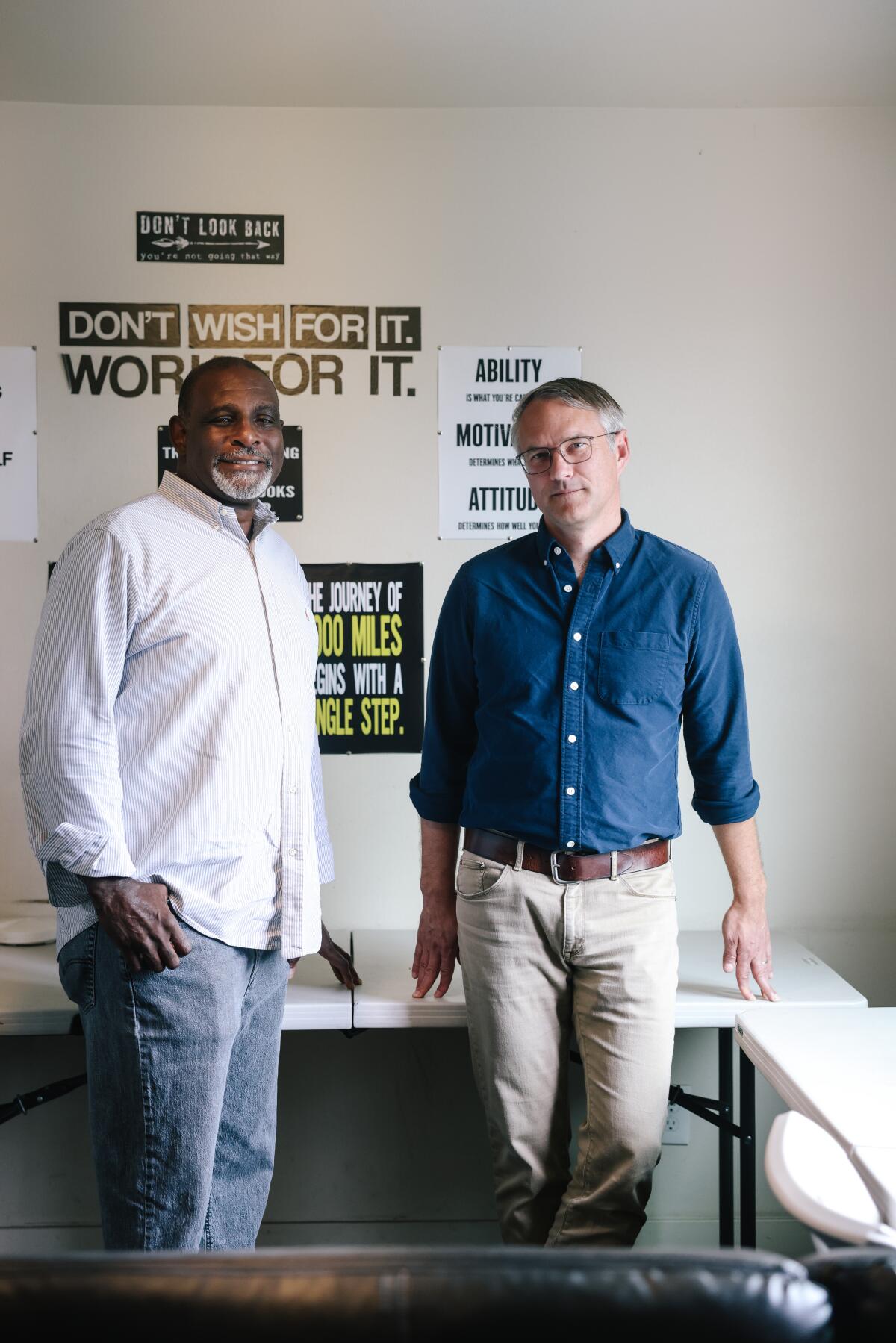 Kalain Hadley, left, and Justin Szlasa stand near desks and signs that read, "Don't wish for it; work for it."