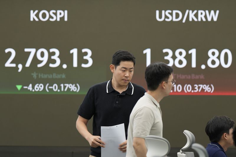 Currency traders walk by the screen showing the Korea Composite Stock Price Index (KOSPI), left, and the foreign exchange rate between U.S. dollar and South Korean won at a foreign exchange dealing room in Seoul, South Korea, Monday, July 1, 2024. (AP Photo/Lee Jin-man)