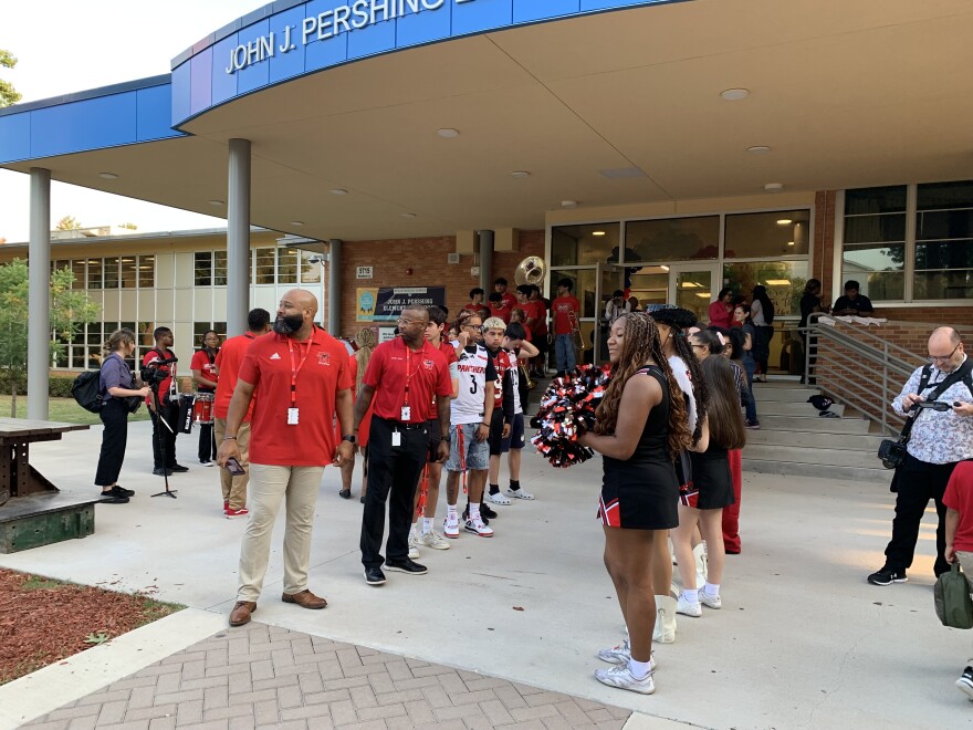 Teachers wearing red polos and cheerleaders form two lines leading into Pershing Elementary school