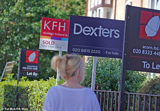 A woman walks past estate agent signs outside homes in Lewisham, South East London (file)