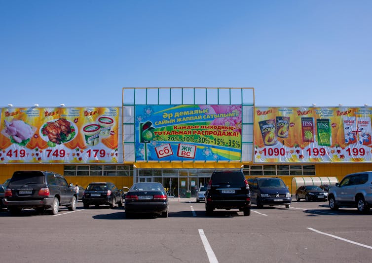 Cars parked outside a supermarket in Astana, Kazakhstan, on a sunny day.