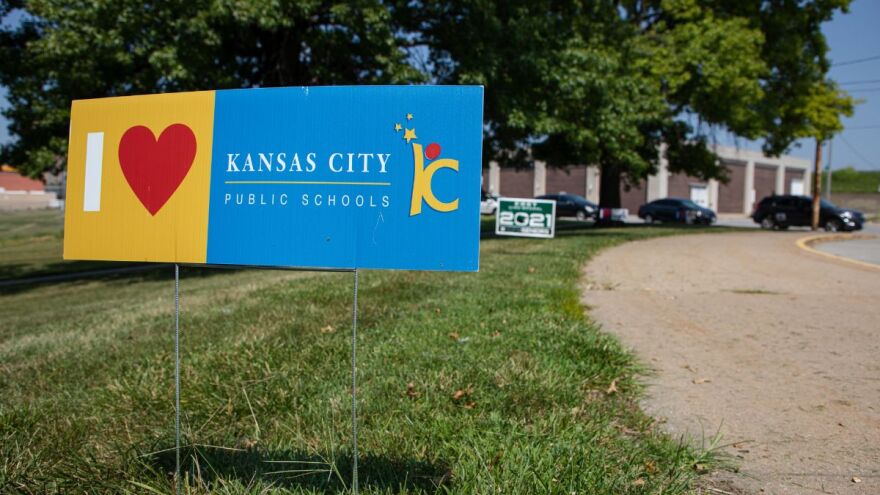 A sign stuck into the grass off a sidewalk says "I (heart symbol) KC Public Schools" with the KCPS logo