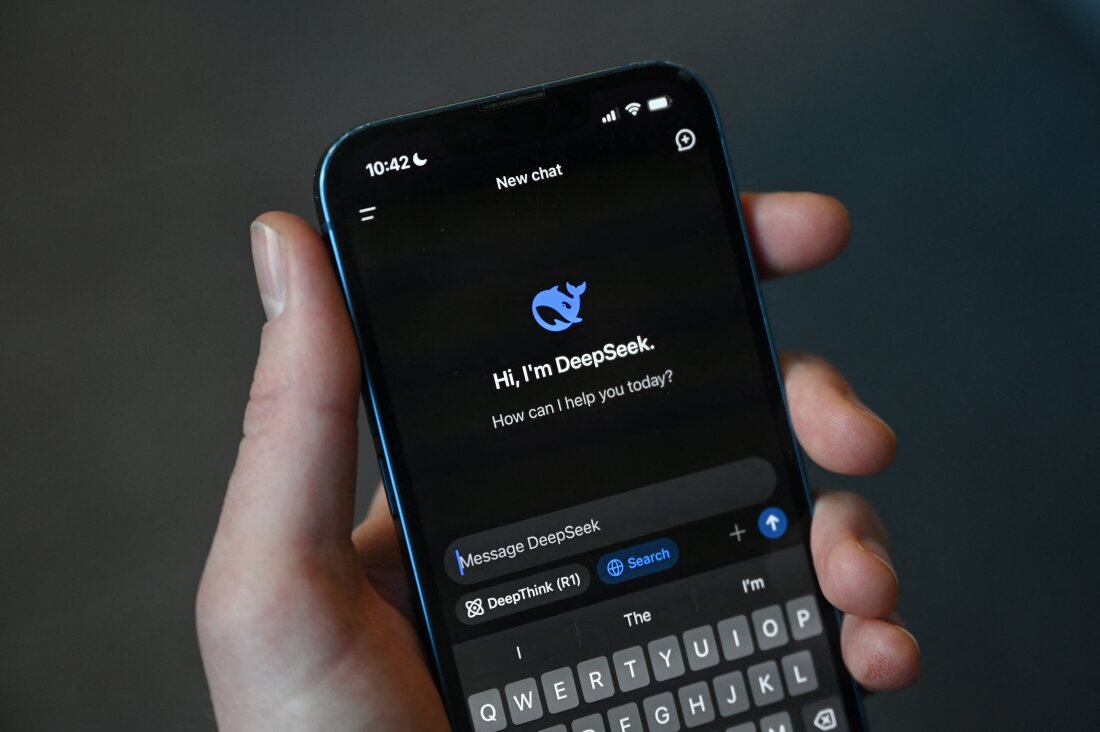 This photo illustration shows a hand holding a smartphone with the DeepSeek app displaying. The app shows DeepSeek's whale logo and displays text saying: "Hi, I'm DeepSeek. How can I help you today?"