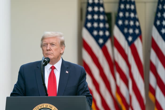 Donald Trump stands at a podium with American flags displayed in the background.