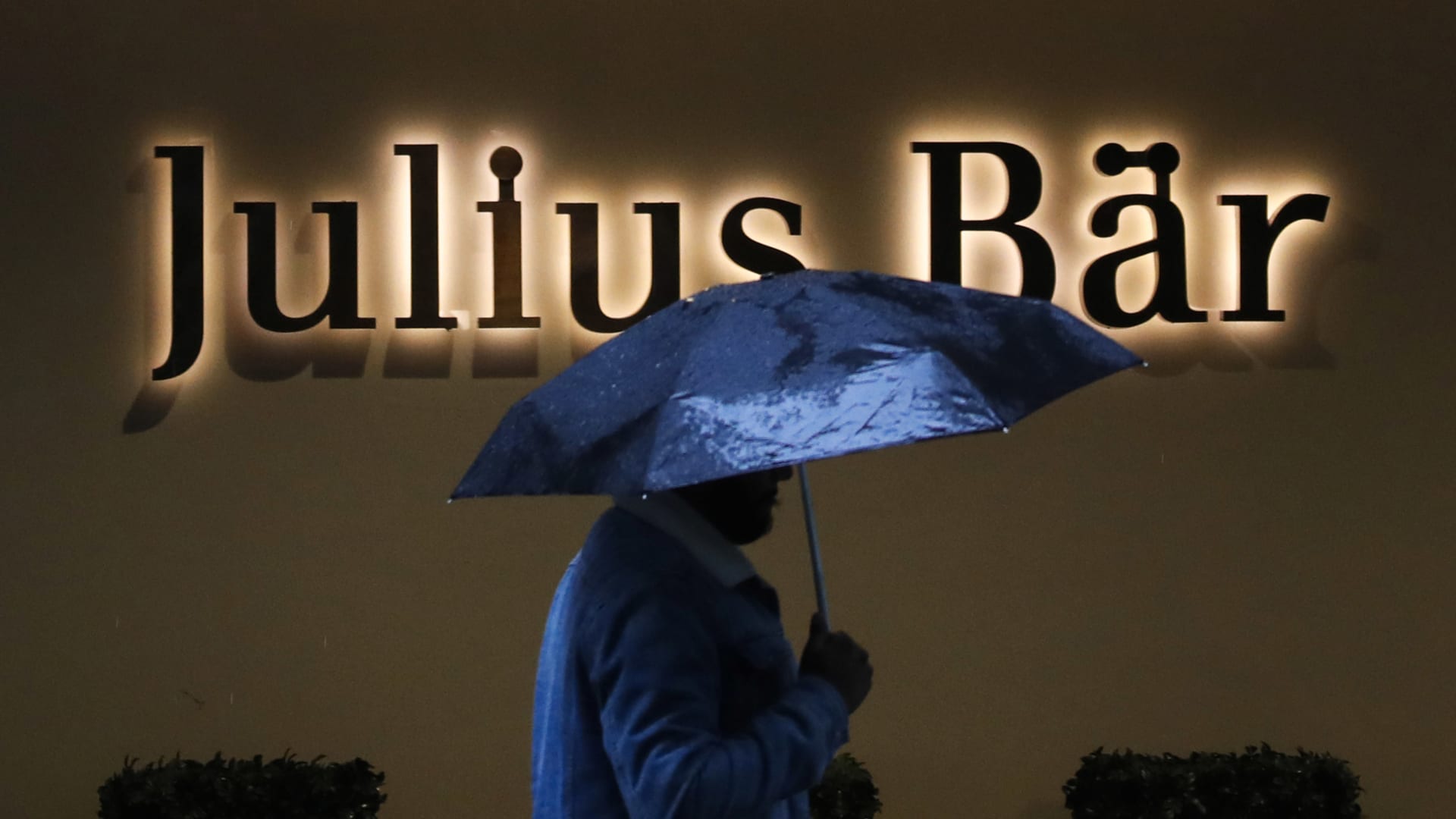 A pedestrian sheltering under an umbrella passes a Julius Baer Group Ltd. branch in Zurich, Switzerland, on Tuesday, July 13, 2021.