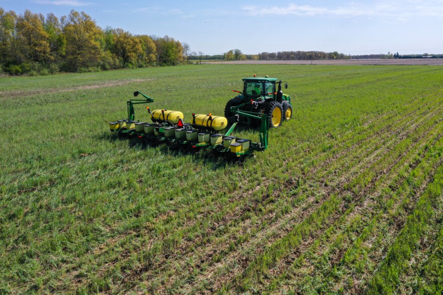 A tractor pulls a seeder through a field with green vegetation.