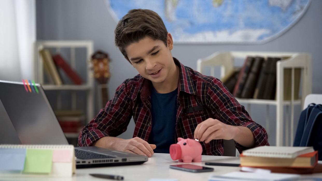 Male kid putting coin into piggy bank, properly saving pocket money, finance