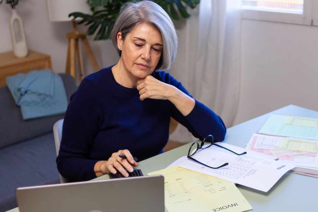 Worried mature woman using calculator and laptop for managing domestic finances and invoices