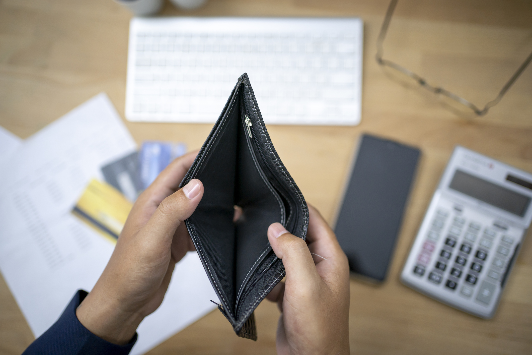 person looking at empty wallet with desk supplies including glasses and calculator in the background
