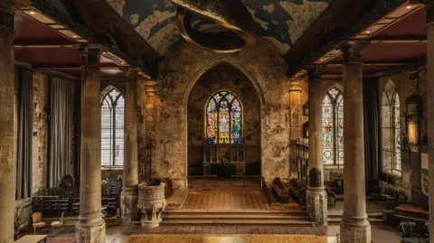 Evoke Pictures The interior of an old church. There are pillars and pews and colourful stained-glass windows at the rear.