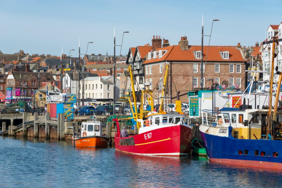 Colourful scene around the harbour in the historic seaside town of Scarborough on the east coast of England. Popular with holidays makers and daytrippers the town has many attractions. Traditional fishing boats moored beside the seafood stalls. Sept 2016.