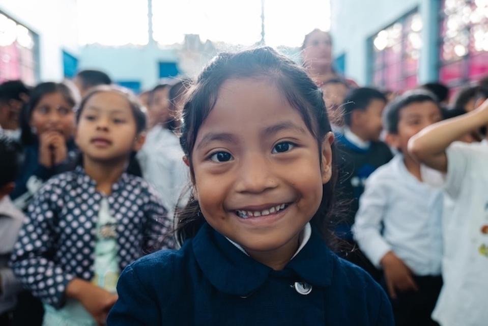With her classmates in the background, a little girl smiles at a school in Guatemala.