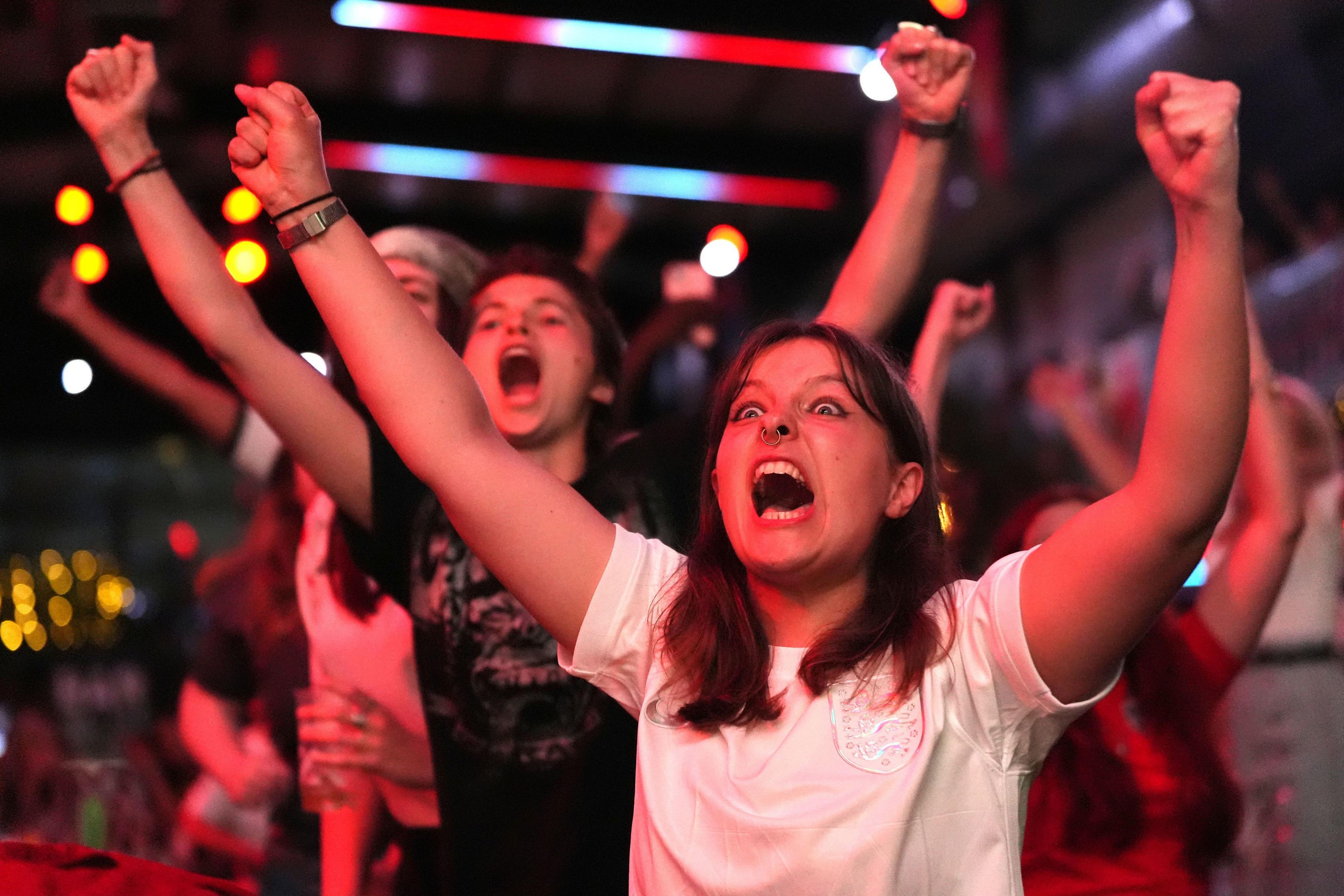 a group of fans put their hands in the air with delight as they watch the penalty shoot out