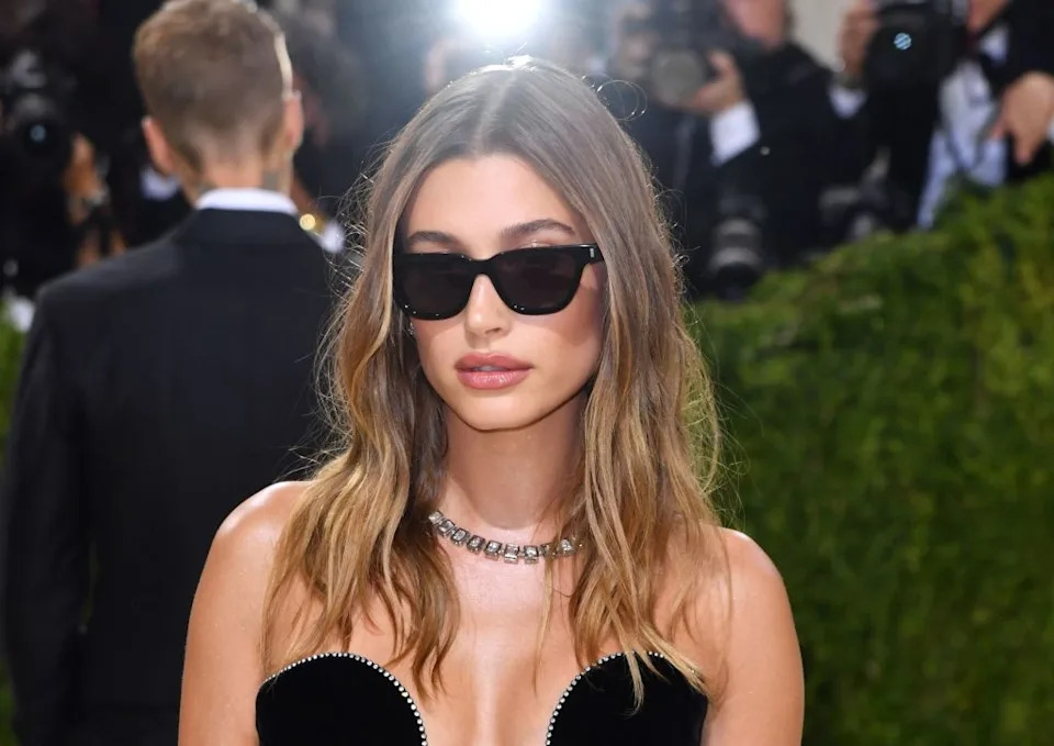 Person in stylish strapless dress and sunglasses on the red carpet, surrounded by photographers