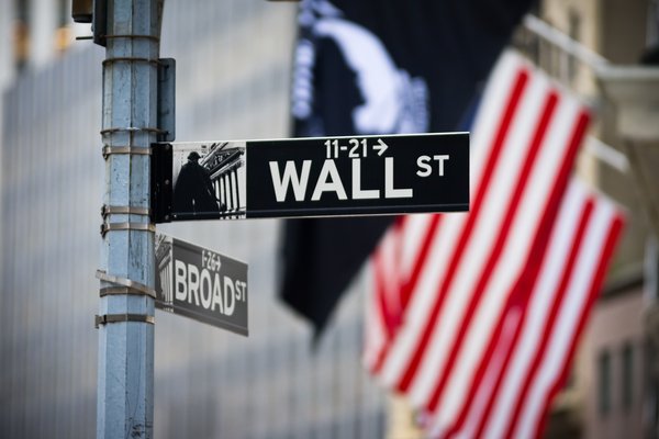 Photo of the Wall Street street sign with American flag in the background.
