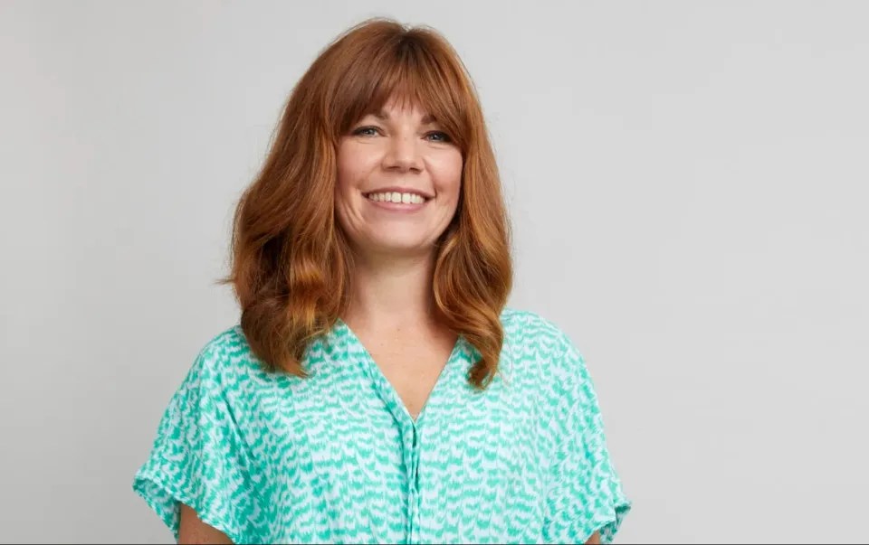 Portrait of a smiling woman with auburn hair wearing a teal patterned shirt.