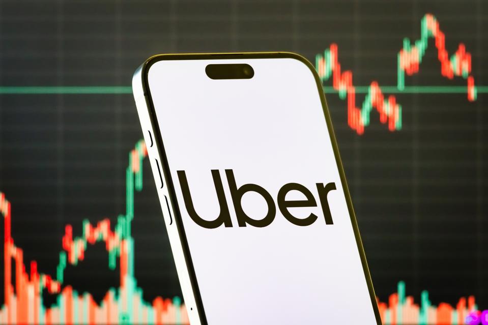 Uber Technologies Inc. logo on smartphone with stock market chart background