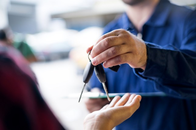 A car salesperson handing out car keys to a buyer at a dealership.