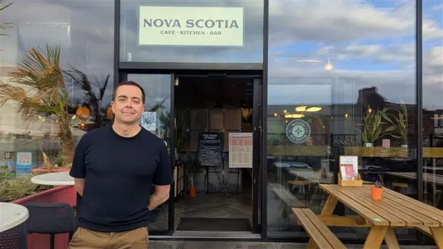 A man in a black t shirt standing outside a restaurant