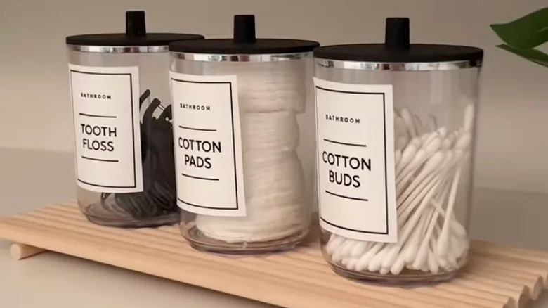 Bathroom storage jars sit on a display shelf made from wooden dowels.