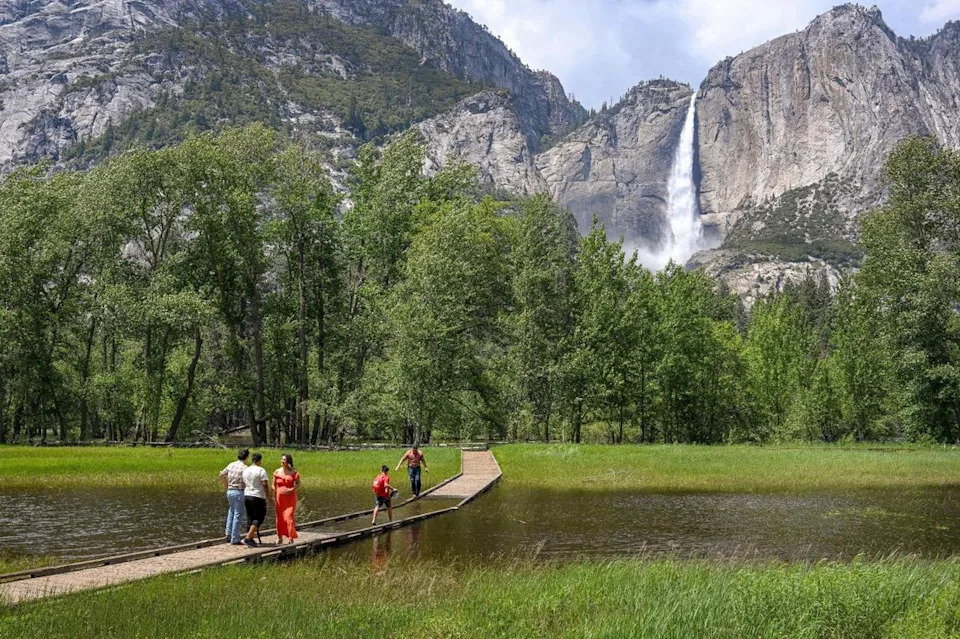 Yosemite National Park visitors contemplate crossing a flooded meadow boardwalk across from Upper Yosemite Falls in Yosemite Valley on Tuesday, June 13, 2023.