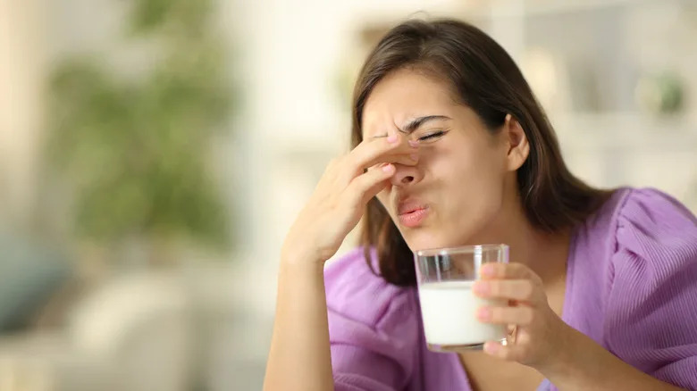 A woman holding her nose over an glass of odd-smelling milk