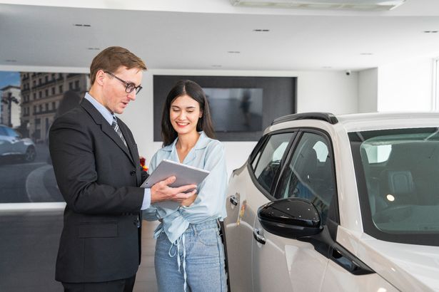 Cheerful car dealership customer talking to auto sales consultant