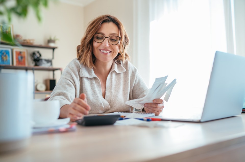 Smiling woman reviewing paperwork and using a calculator at her home office.