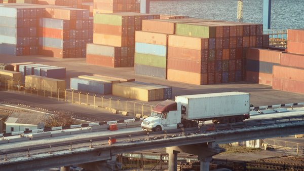Truck drives past docks with cargo containers.