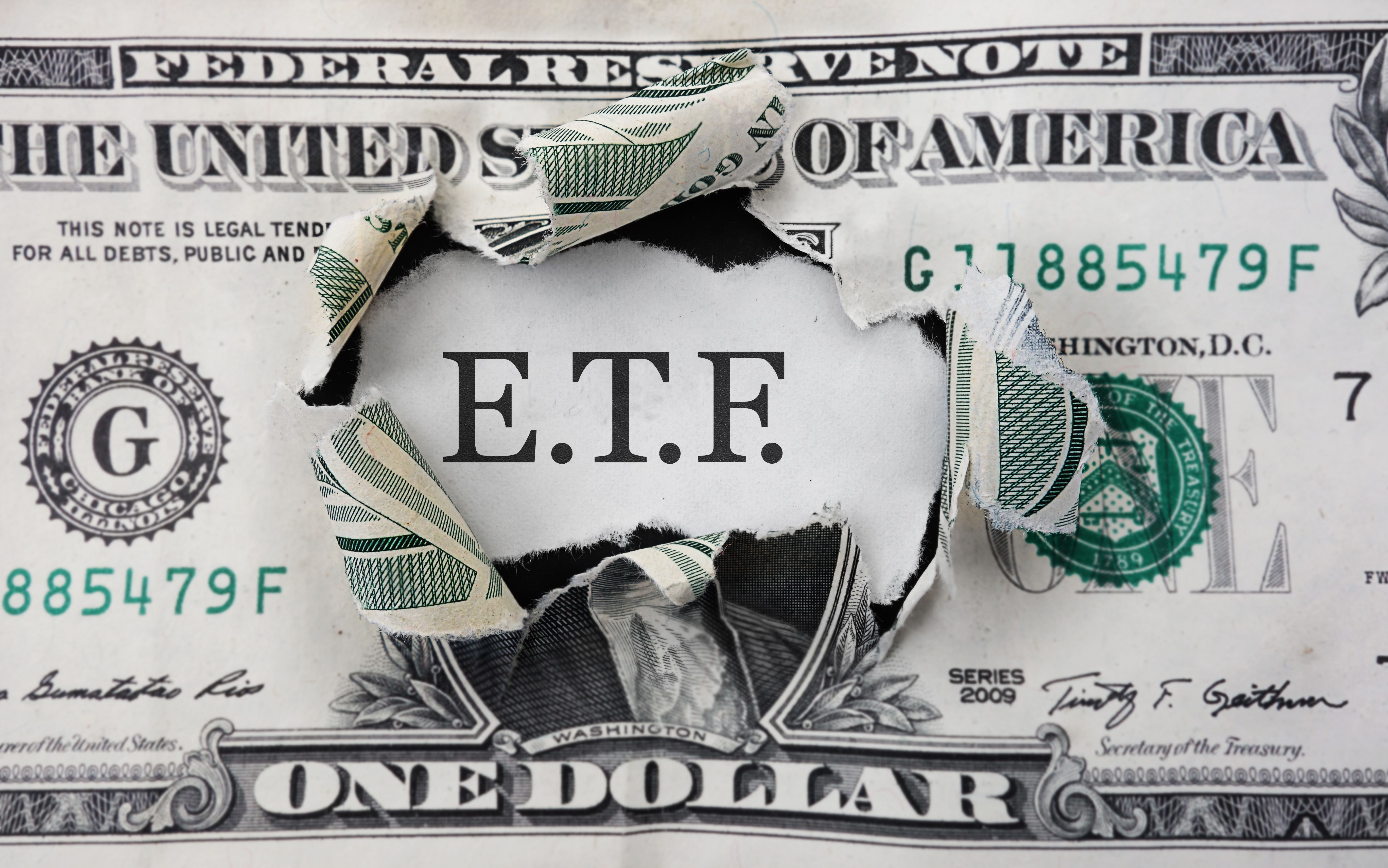The word ETF appears torn through a U.S. dollar bill, representing exchange-traded funds and investing