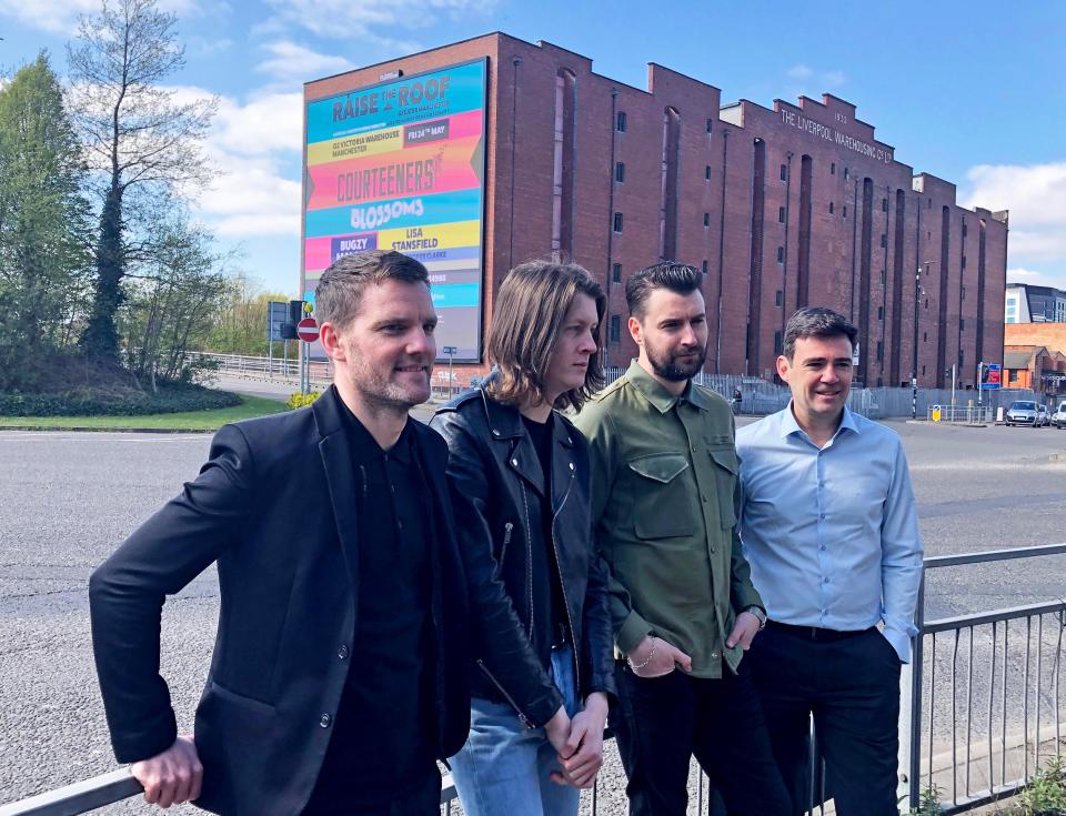 Four men standing in front of a building with a "Raise the Roof" concert banner. From left to right: Tim Heatley, Tom Ogden, Liam Fray, and Andy Burnham.