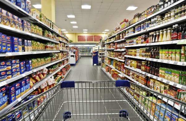 A shopping cart being pushed down a grocery store aisle.