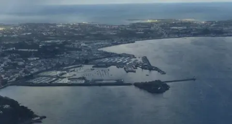 BBC An aerial view of Guernsey, showing part of the island at dusk, with lights on in many buildings, and a harbour