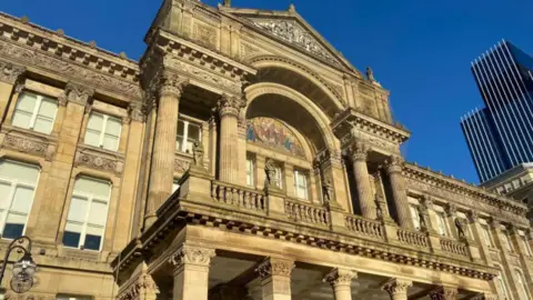 LDRS A view of Birmingham City Council house, with three tall tower block buildings to its right. The building is bathed in sunshine.