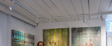Miranda Donovan standing in her London studio beside three mixed-media paintings