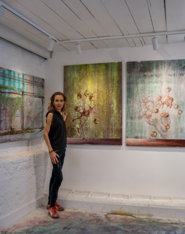 Miranda Donovan standing in her London studio beside three mixed-media paintings