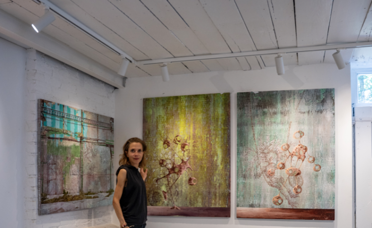 Miranda Donovan standing in her London studio beside three mixed-media paintings