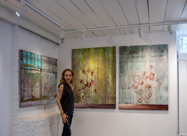 Miranda Donovan standing in her London studio beside three mixed-media paintings