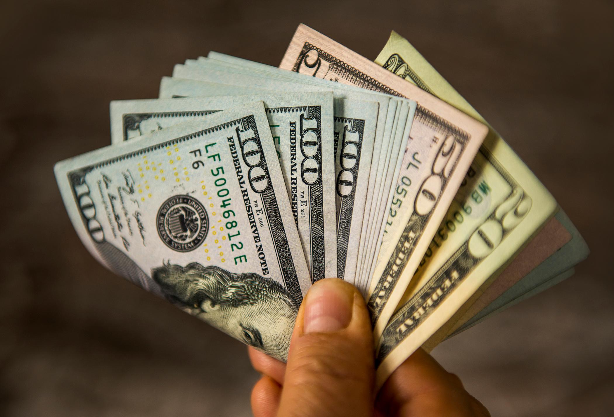 A person holding a fanned and folded assortment of cash bills by their fingertips.